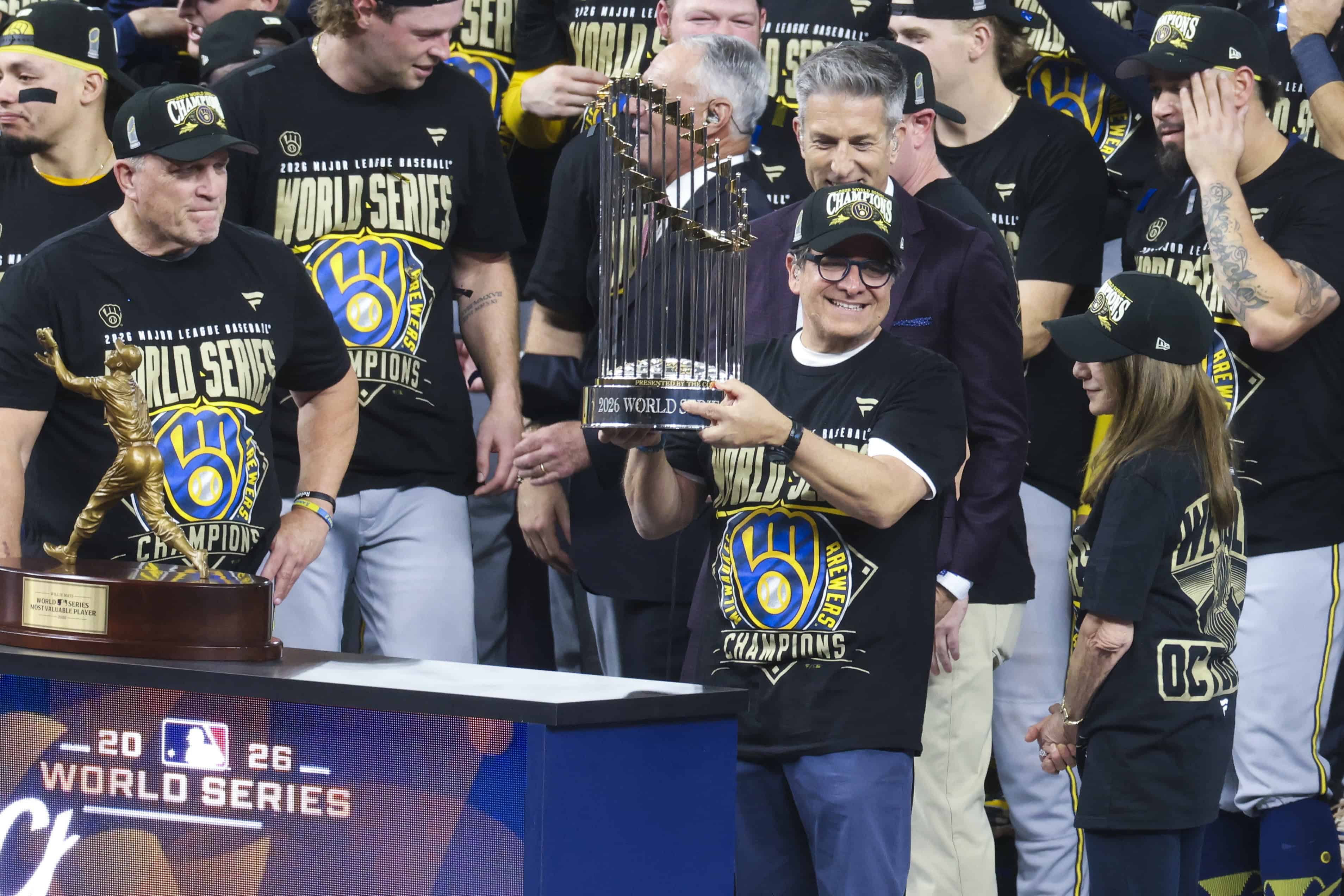 El propietario de los Milwaukee Brewers, Mark Attanasio (C-D), sostiene el trofeo de campeón tras la victoria en el quinto partido de la Serie Mundial de las Grandes Ligas de Béisbol (MLB) antelos Tampa Bay Rays en el Tropicana Field de San Petersburgo, Florida, EE. UU., el 28 de octubre de 2026. 